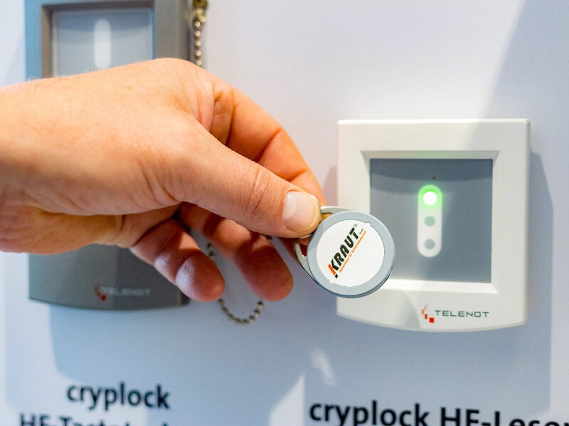 Eine Hand hält einen Schlüsselanhänger mit der Aufschrift KRAUT vor einem Zugangskontrollleser