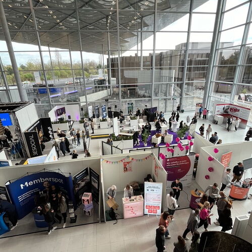Eine Messehalle mit vielen Ständen und Besuchern, die sich unter einem Glasdach bewegen