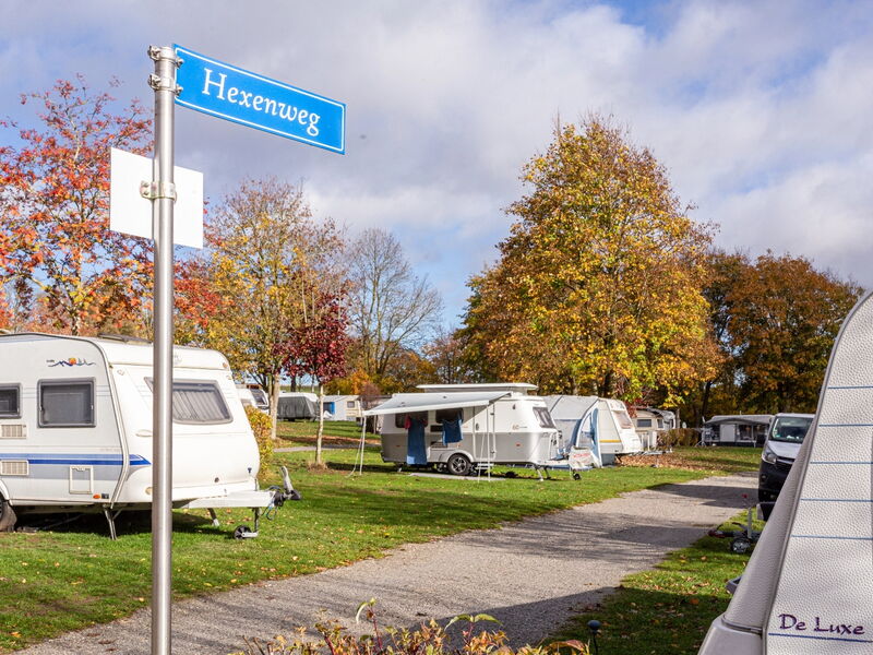 Wohnwagen auf einem Campingplatz im Herbst mit bunt gefärbten Bäumen und einem Straßenschild