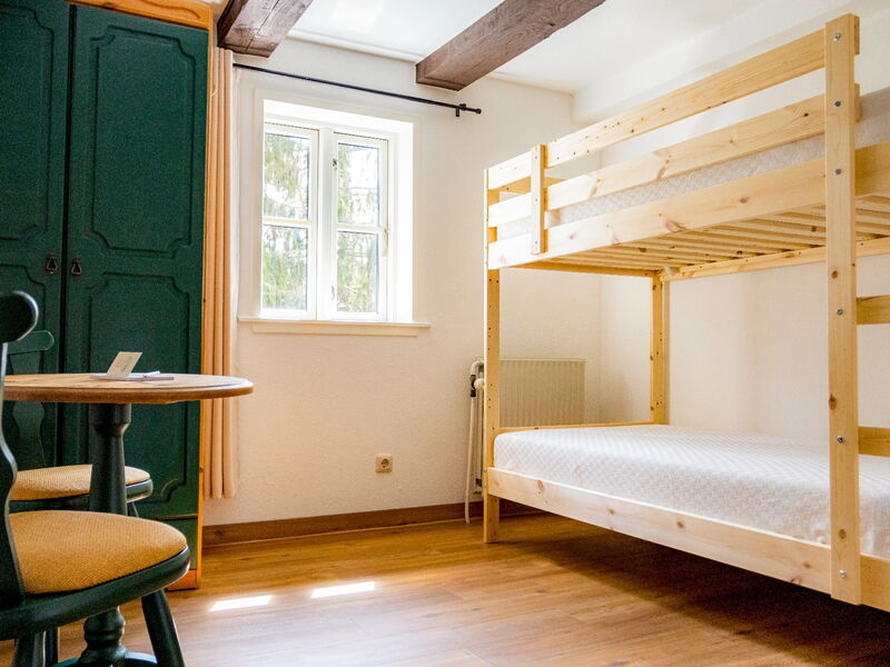 Ein Zimmer mit einem Holzbett, einem grünen Kleiderschrank, einem runden Tisch mit zwei Stühlen und einem