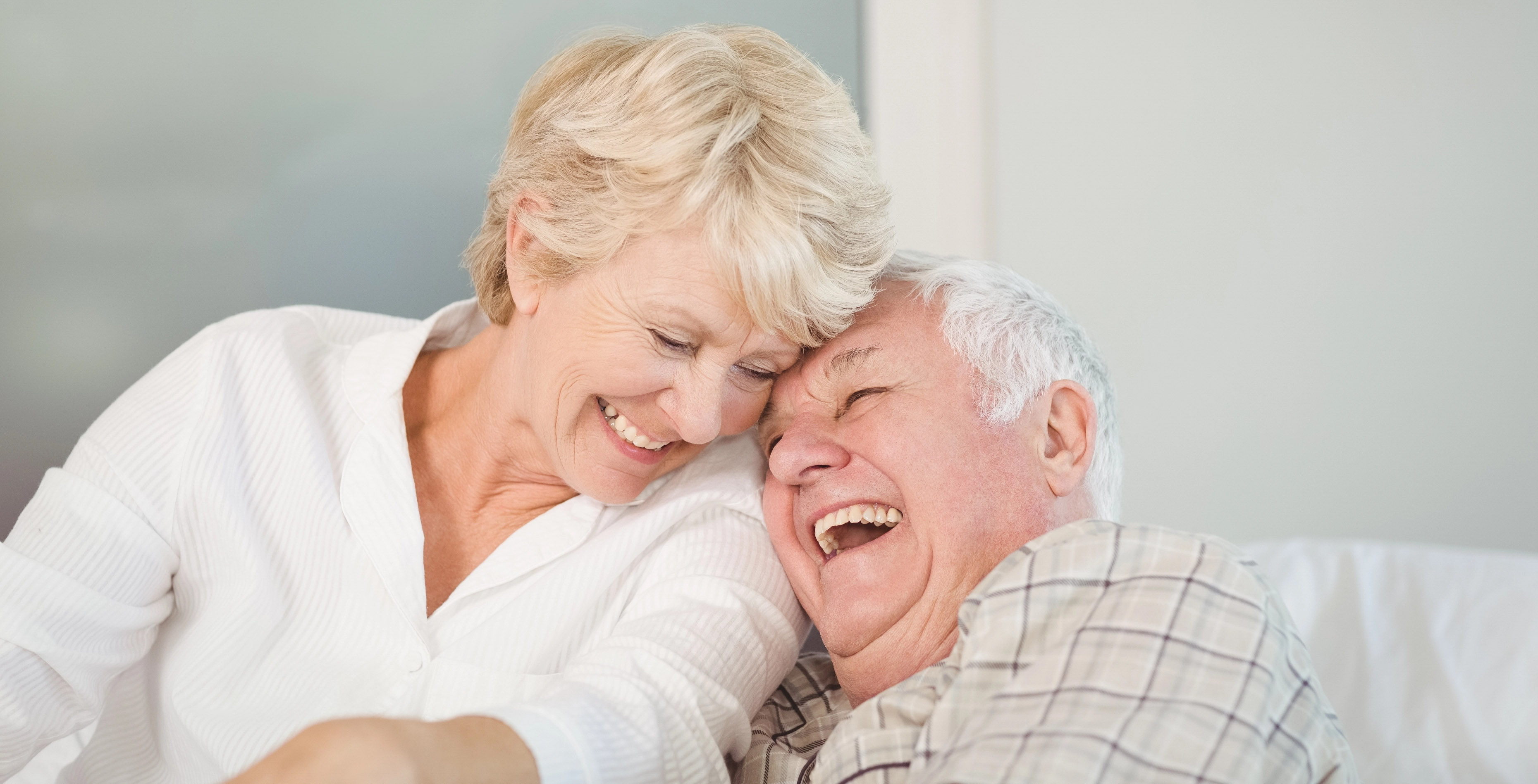 Ein älteres Paar lacht herzlich, die Frau lehnt ihren Kopf an den Mann